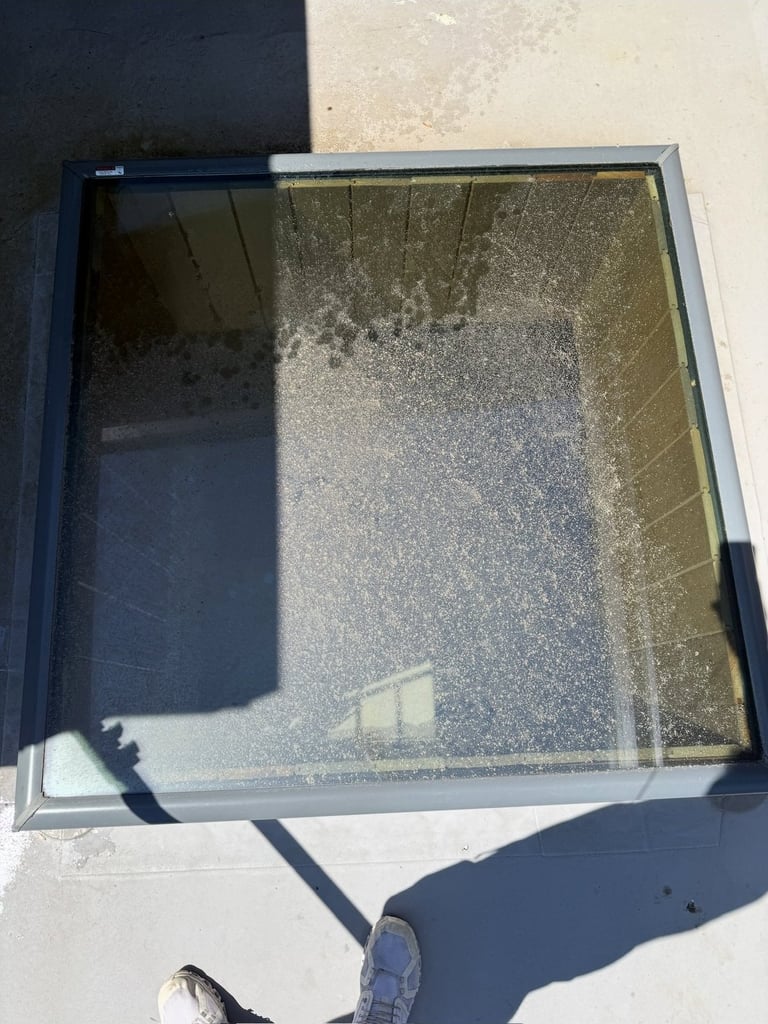 Overhead view of a flat roof skylight with dust and debris accumulation on its glass surface casting shadows