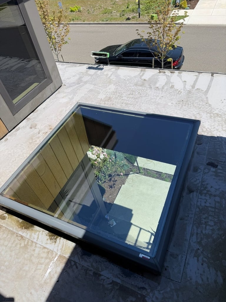 Overhead view of an open basement window well with blue frame, showing interior stairs and a black car parked on the street above