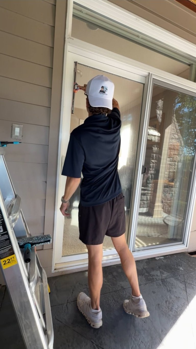 Person wearing white cap and black hoodie standing at glass sliding doors with white sneakers visible.