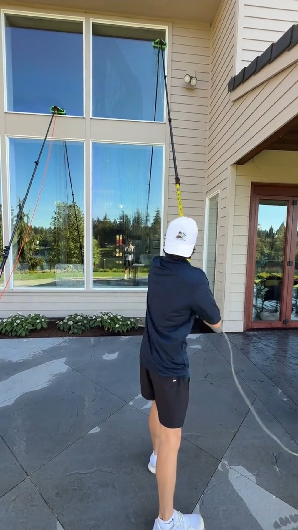 Person in white cap and dark shirt jumping rope on patio in front of large windows and residential house